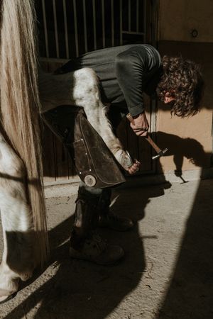 Man shoeing horse near stable