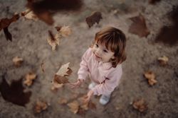 Joyful child scattering leaves on lawn in park