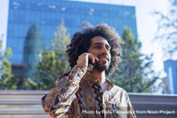 Handsome smiling man with curly hair using a mobile phone while standing outdoors 5r9zp3