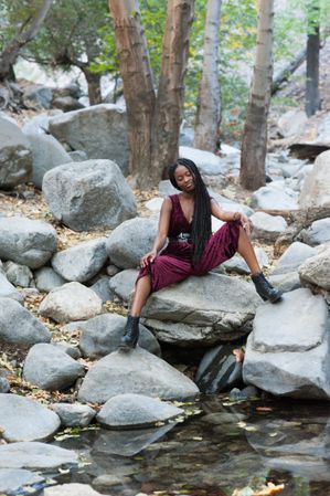Woman sitting on boulders over a creek in red jumpsuit