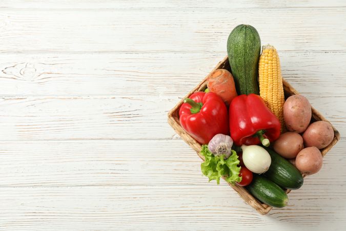 Wicker basket with vegetables on wooden background, copy space