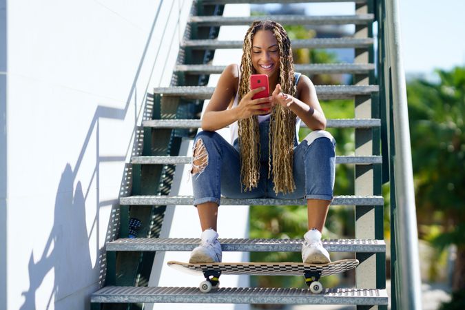 Smiling female skater texting on phone on stairs, copy space