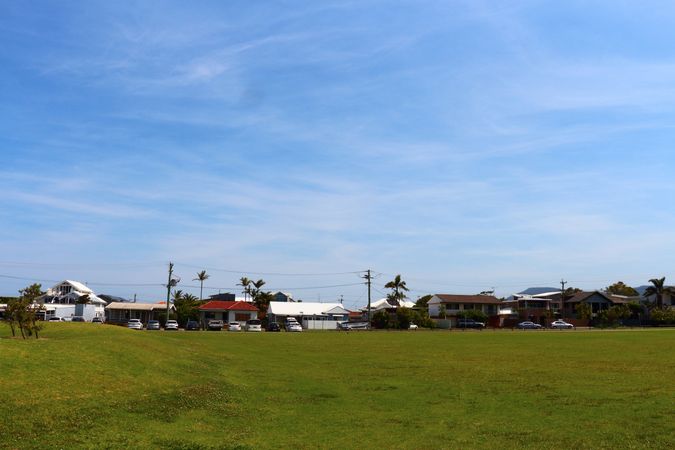 Suburban Houses Next To Open Green Field Under A Clear Blue Sky On A Sunny Day