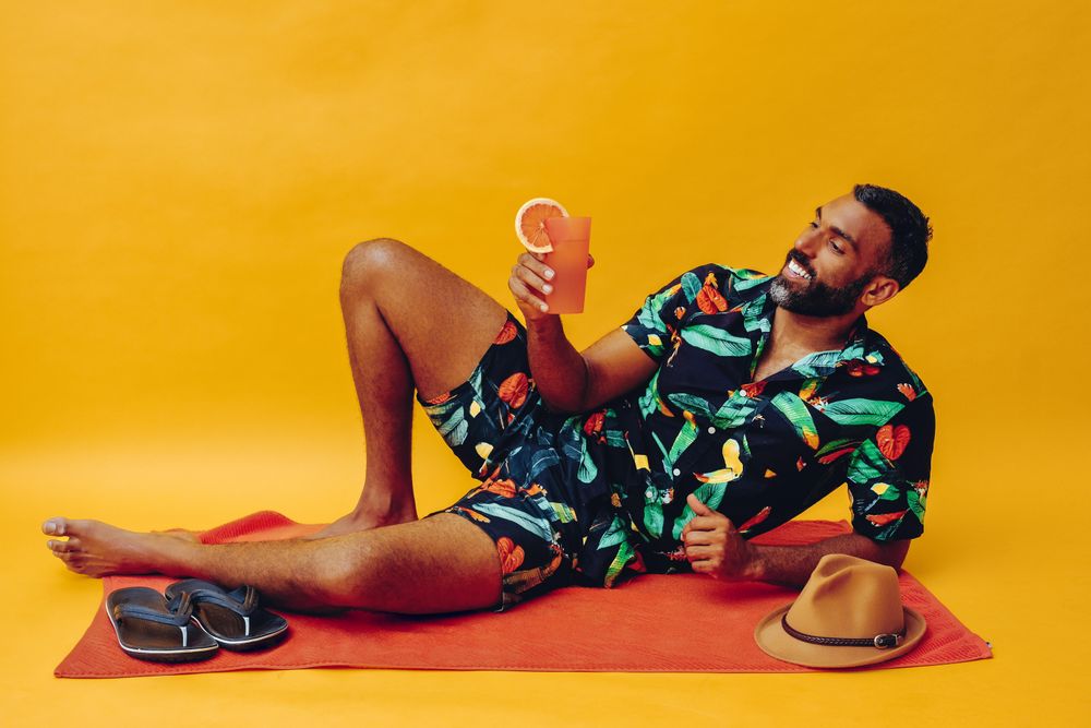 Black male laying back on towel and smiling while holding tropical drink