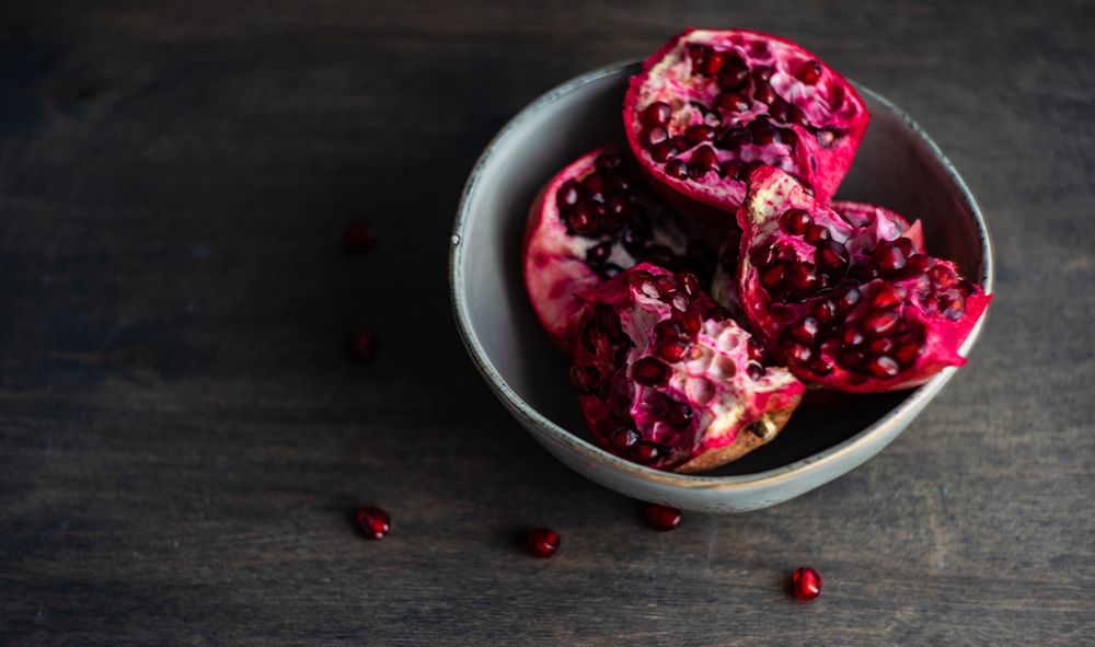 Ceramic bowl of open pomegranates on wooden table