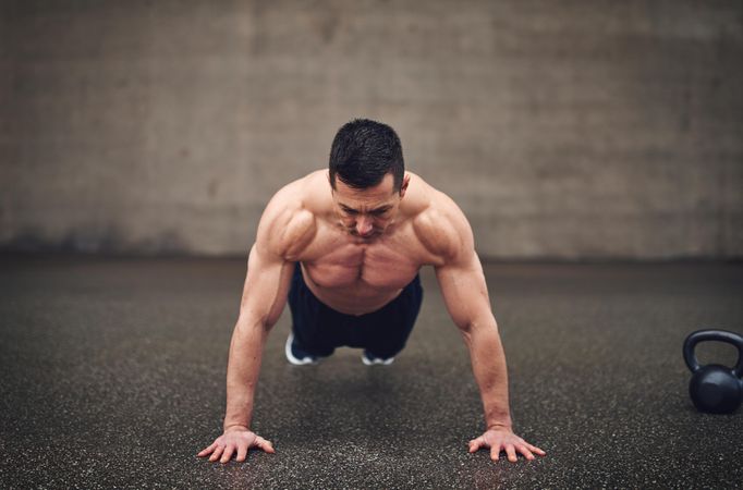 Fit shirtless man doing planks in concrete space