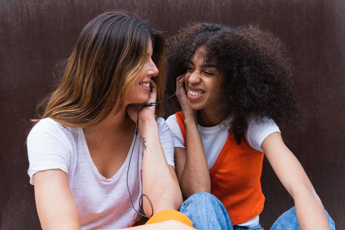 Smiling diverse girlfriends listening to music with earphones