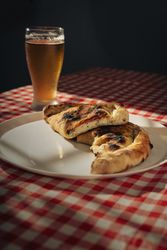 Calzone and beer served on plate over checkered table