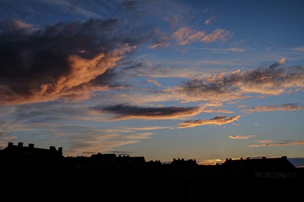 Blue sky with colorful clouds over houses in the shadows