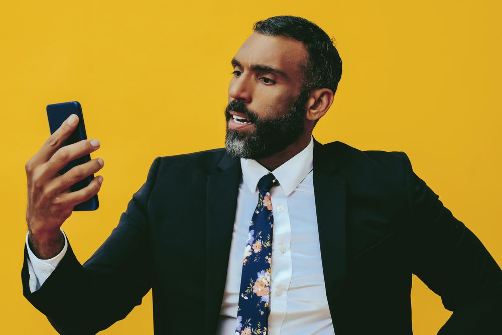 Agitated Black businessman in suit speaking at smartphone screen