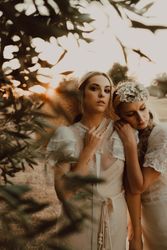 Charming slim brides with flowers in garden with olive trees