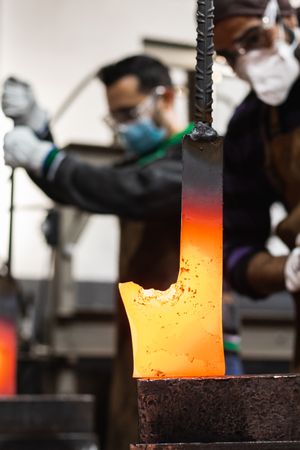 Blacksmiths forging hot metal with hammer in workshop