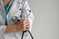 Crop physician with stethoscope on light background