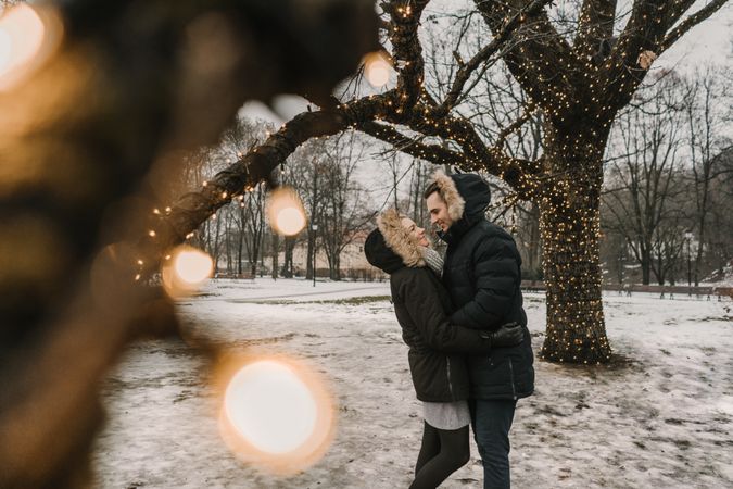 Smiling couple having fun on street near tree with fairy lights