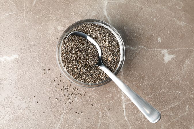 Glass sauce boat with chia and spoon on textured background, top view