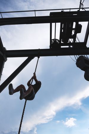 Anonymous man climbing rope in outdoor gym