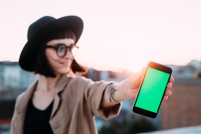 Woman at dusk with glasses and hat with smart phone outside