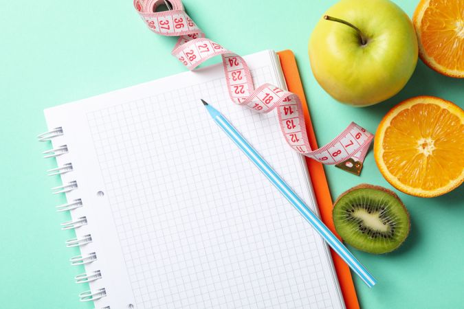 Notebook, measuring tape, pen and vegetarian food on mint background. Weight loss