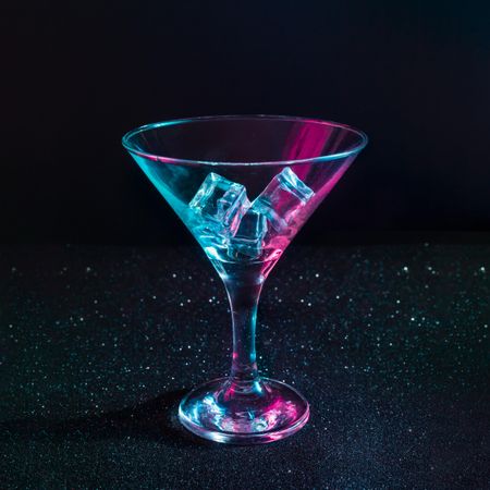 Martini cocktail glass with ice cubes in neon iridescent pink and blue colors