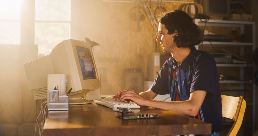 White Male Software Engineer Programming On Old Desktop Computer In Retro Garage With Random Appliances.
