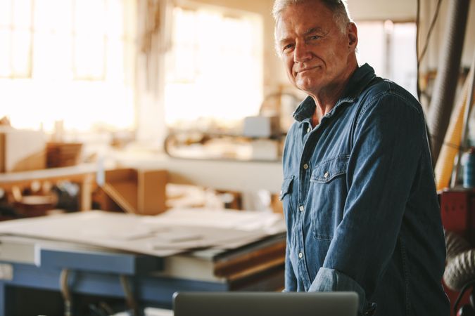 Mature male carpenter looking at camera standing in workshop