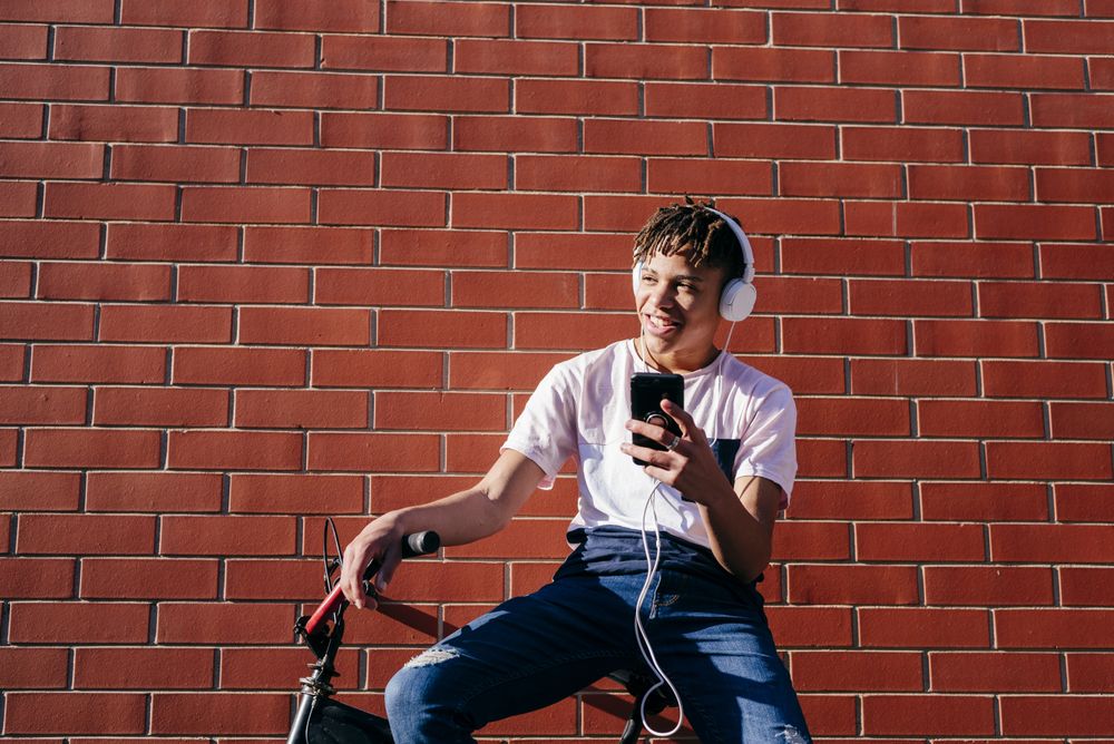 Young happy Black male listening music with smartphone on bike