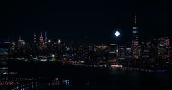 Scenic Aerial New York City Night View of Manhattan Architecture and Big Shining Full Moon. Panoramic Financial District Photo from a Helicopter. Cityscape with Office Buildings and Skyscrapers
