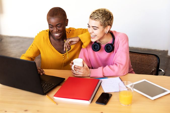 Two female friends studying at laptop together with coffee