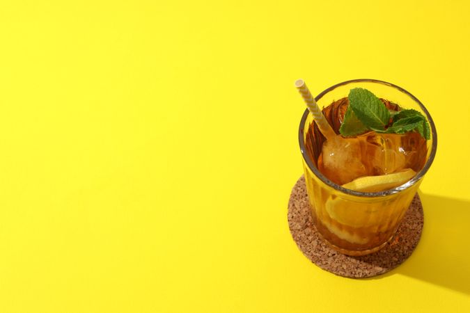 Cold tea with orange slices and mint leaves on a yellow background