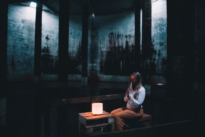 Woman with praying hands near lamp on bench in building