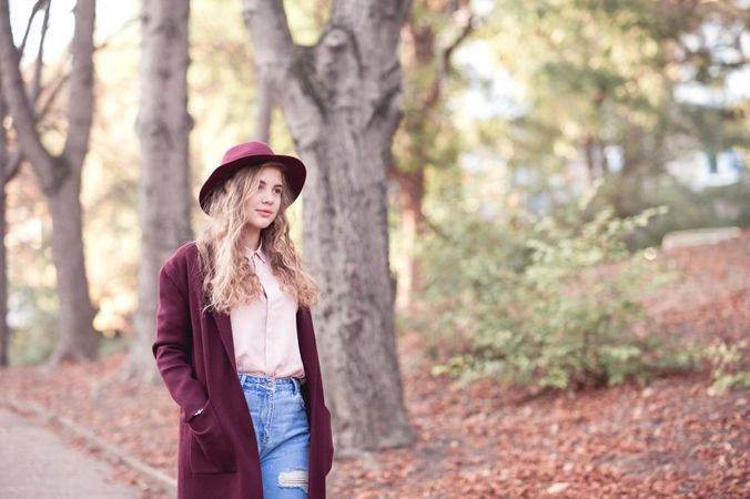 Teenage girl in purple coat and hat walking near trees outdoor