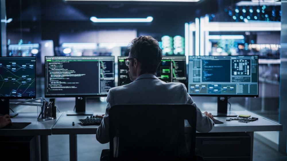 Back View of a Young Engineer Working on Computer in a Technological Office Environment. Male Programmer Writing Software Code for a Blockchain Project, Developing Backend System