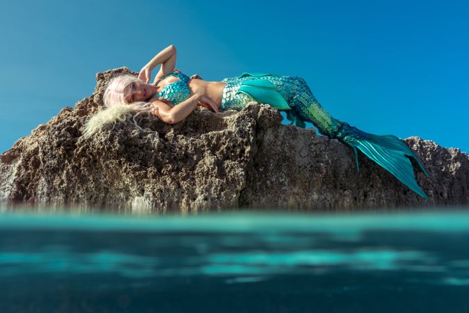 Blond fairytale female mermaid lying on rock