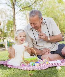 Grandfather and Granddaughter Coloring Easter Eggs on Blanket At Park