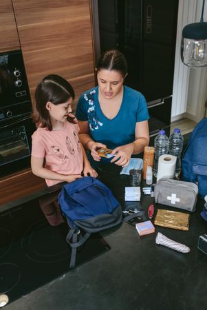 Mother preparing emergency backpack with her daughter