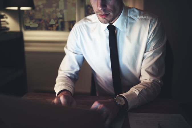 Businessman in shirt and tie typing on laptop at night