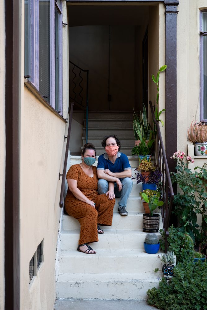 Man and woman sitting on stairs in front of apartment looking at camera