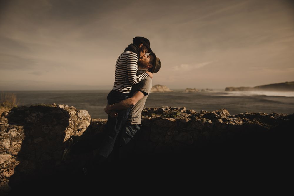 Man kissing and holding woman on hands near stones on shore