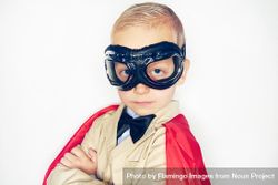 Serious blond boy wearing airplane goggles and cape with arms crossed 48kGR5