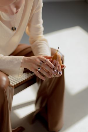 Cropped image of woman in brown leather pants sitting and holding a pear
