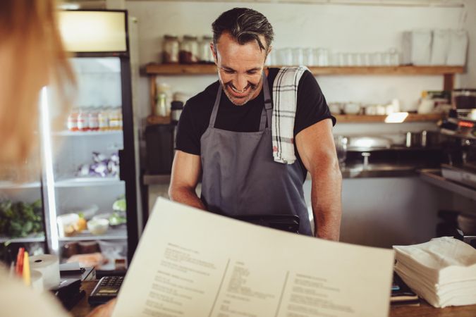 Male barista standing at cafe counter entering customer order on computer
