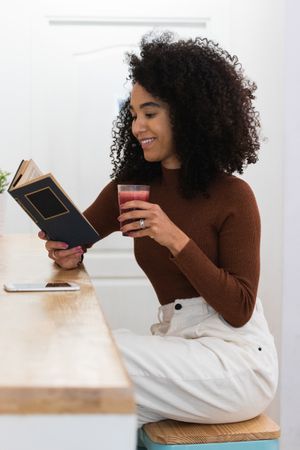 Black woman drinking smoothie and reading book in bar
