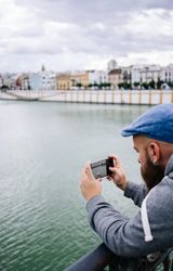 Guy on vacation in casual clothing making photo of bay on smartphone at quay