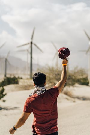 Man holding hat up and standing beside wind turbine field