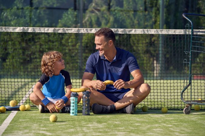 Cheerful coach with boy sitting on court