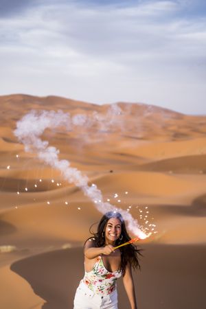 Happy woman holding firework in desert