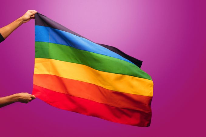 Cropped shot of hands holding pride flag against purple background