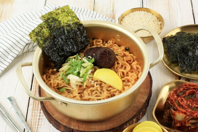Brass pot full of noodles with seaweed, radish, onion and mushroom garnish