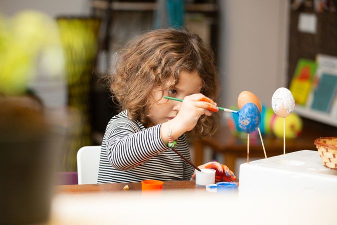 Toddler girl painting egg at table