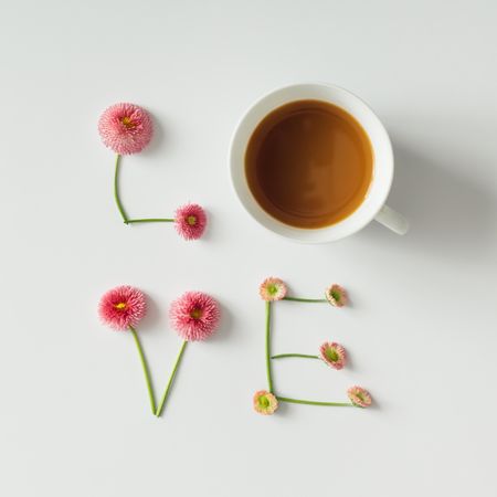"Love" made of flowers and coffee cup on light background